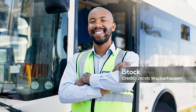 A bus driver standing smiling in front of a bus