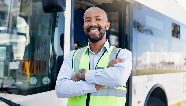 A bus driver standing smiling in front of a bus