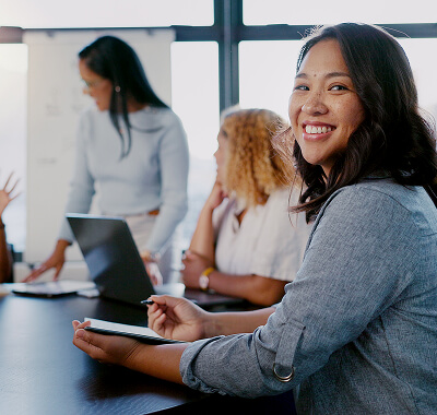 A woman sitting in a meeting, smiling to camera
